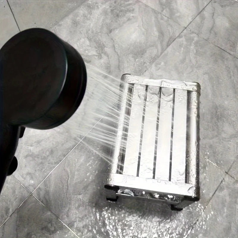 Metallic shower head spraying water onto a metal tray on a tiled floor.